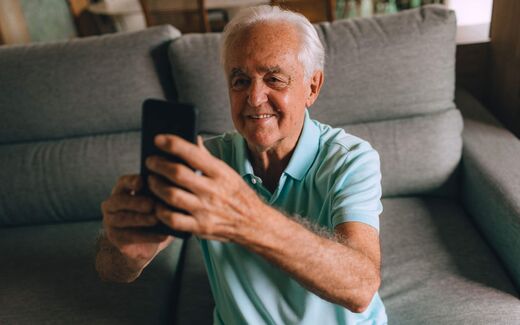 An older adult viewing a smartphone at home, a stand-in for a patient using a prescription drug companion app
