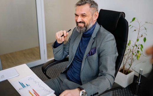 A gray-haired executive in a blazer smiles while reviewing bar and line charts on a printed report