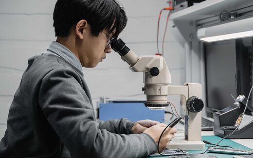 A technician examines a circuit board under a stereo microscope, a generic stand-in for Elucid Bioimaging