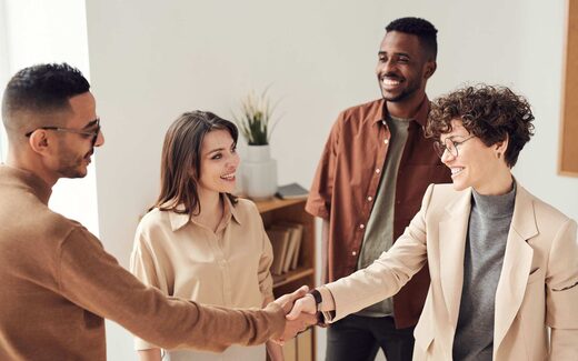 Four colleagues shake hands and smile in a bright office setting