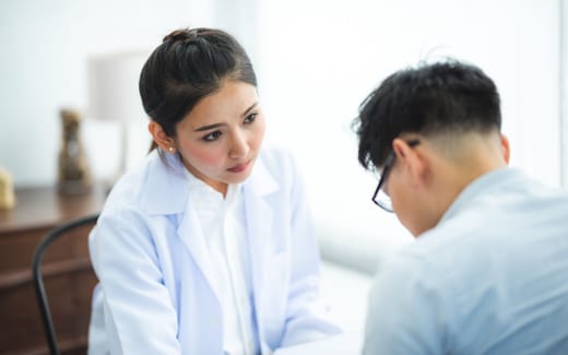 A physician in a white coat listens closely during a consultation with a patient in a bright exam room