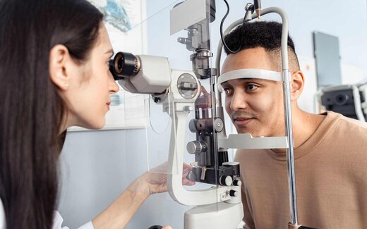 An ophthalmologist examines an adult patient's eye at a slit lamp during a clinic visit