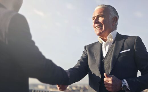 Two colleagues shake hands outdoors against a bright sky
