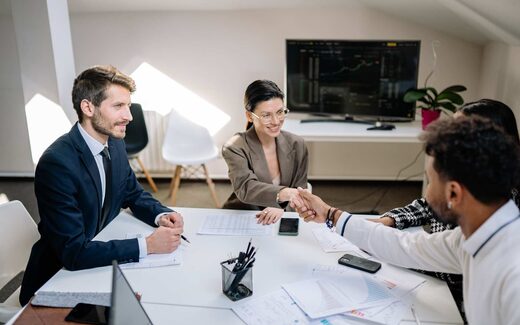Two colleagues shake hands across a table in a bright office