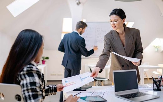 A team of colleagues reviews a chart and hands off a printed report during a planning session in a bright loft office