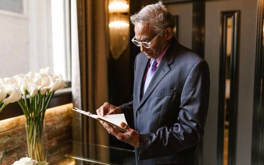 A senior professional in a pinstripe suit reads a clipboard document closely in a sunlit building lobby
