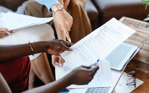 Two colleagues review a printed self-injection instruction sheet next to an open laptop