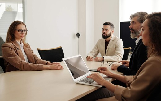 Colleagues around a conference table lean in as one reviews a document, in the middle of a close discussion