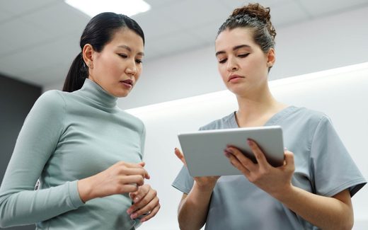 A nurse holding a tablet consults with a colleague in a bright white clinic hallway