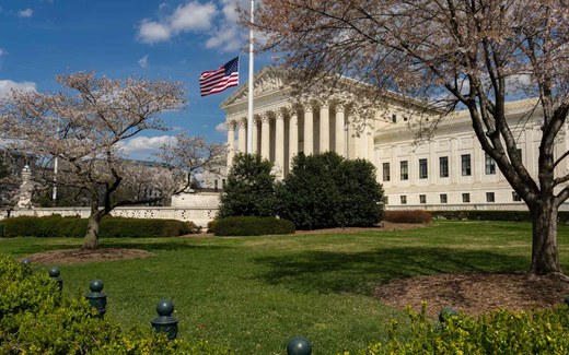 The U.S. Supreme Court Building in Washington, D.C., framed by blooming cherry trees under a clear blue sky