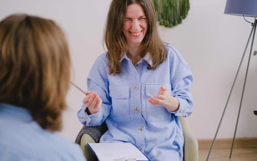 A woman laughs mid-conversation while holding a clipboard during a bright, informal consultation