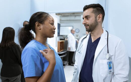 A doctor and nurse confer in a hospital corridor
