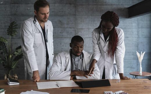 Three physicians in white coats review a patient's chart and medication together at a desk