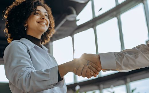 Two colleagues shake hands in a sunlit glass atrium, sealing a deal
