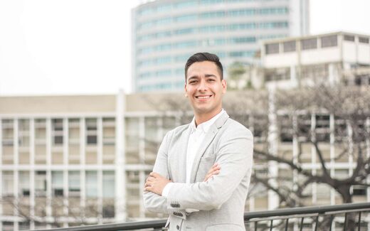 A smiling business professional standing on a city balcony, representing icotec's device-industry leadership