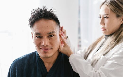 A clinician examines a patient's skin near the hairline in a clinic, a generic stand-in for a skin check