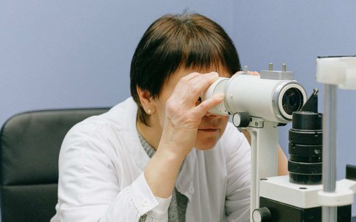 A clinician in a white coat examines a patient at an ophthalmic slit lamp
