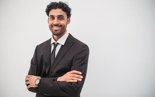 A smiling physician in a dark suit, standing in for GSK's leadership announcing the Jemperli rectal cancer approval
