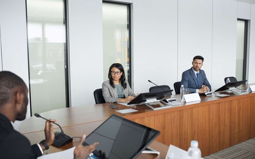 Colleagues seated at a conference table with microphones review documents during a panel discussion