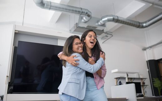 Two women in an office embrace and laugh together in celebration
