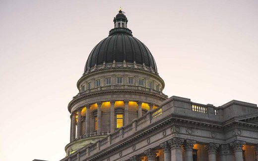 The illuminated dome of the Utah State Capitol building at twilight against a soft pink sky