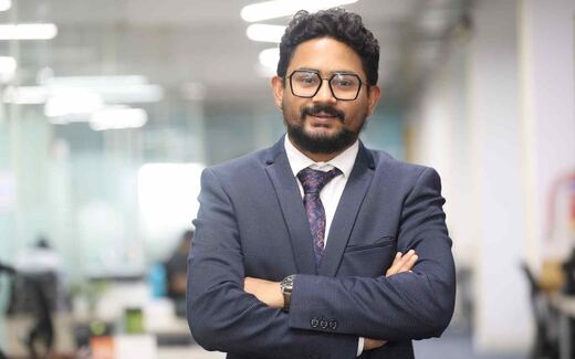 A confident executive in a navy suit, arms crossed, standing in a bright open-plan office