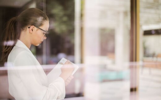 A clinician in a white blouse reviews notes reflected in a glass partition in a bright office