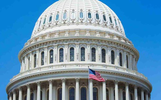 The dome of the U.S. Capitol rises against a clear blue sky, an American flag flying from its balustrade