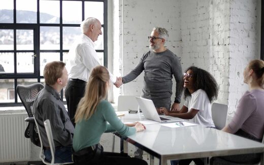 Colleagues shake hands around a conference table in a bright loft office