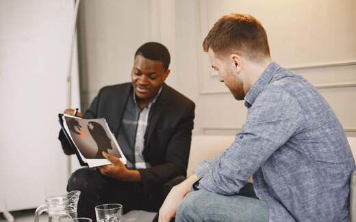 A counsellor shows a client an illustrated guide to mental health risks during a consultation in a bright room, standing in for the antidepressant safety review