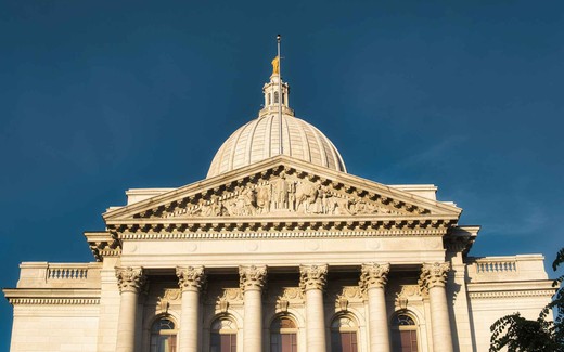 A low sun lights the dome and pediment of a neoclassical government capitol building against a deep blue sky