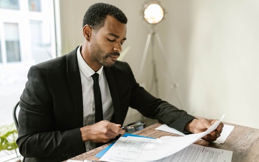 A man in a suit reviews a document closely with a magnifying glass