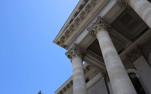 Looking up at the columns and carved pediment of a neoclassical courthouse against a clear blue sky