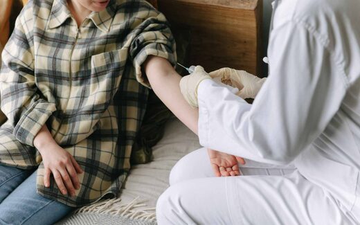 A clinician administers an injection into a patient's arm during a home visit, a generic stand-in for vaccine administration