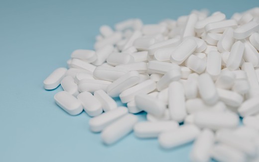 A loose pile of white, oblong pharmaceutical tablets spread across a light blue background