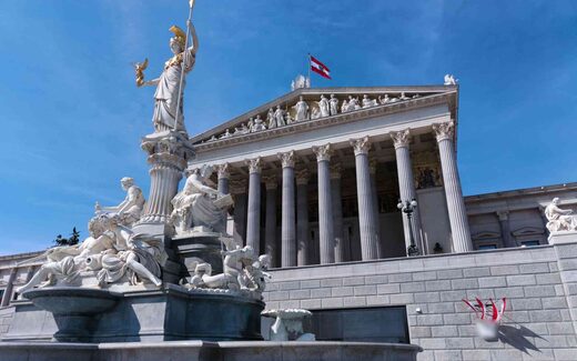 The Austrian Parliament building in Vienna behind the Athena fountain under a clear blue sky, a generic European-institutional stand-in
