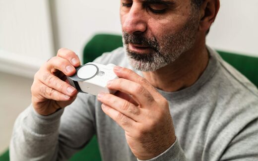 A man closely examines a small white electronic medical device held in both hands