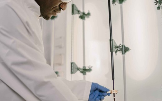 A researcher in a white lab coat and blue nitrile gloves handles laboratory titration equipment while wearing safety glasses