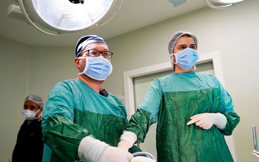 Two surgeons in green gowns and masks in a bright operating room, a generic stand-in for a transcatheter valve-repair procedure
