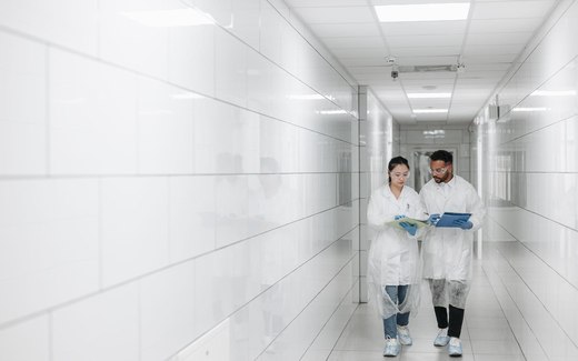 Two gowned staff walking and reviewing notes together in a bright cleanroom corridor
