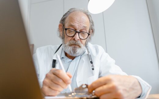 A physician in a white coat reviews a patient's chart on a clipboard