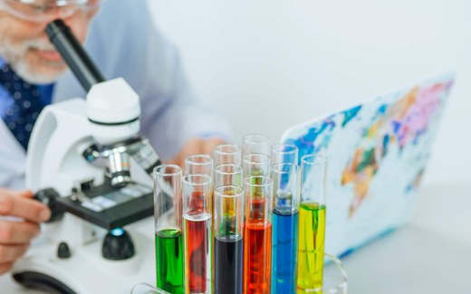 A scientist examines colorful test tubes and vials under a microscope in a laboratory