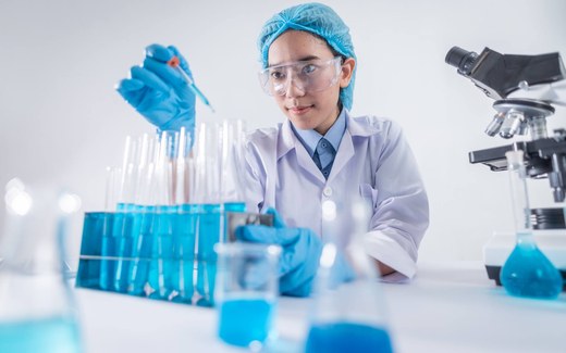 A laboratory scientist in blue nitrile gloves uses a pipette over a rack of test tubes