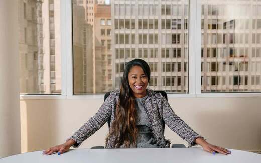 A senior executive smiles at the head of a boardroom table with a city skyline behind