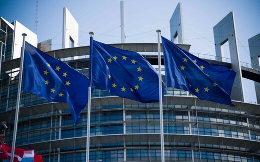 European Union flags flying in front of the European Parliament building in Strasbourg under a clear sky