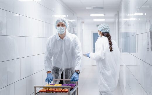 Lab staff push a sample cart through a bright cleanroom corridor