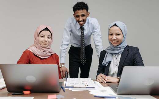 Three colleagues at laptops reviewing a printed chart-filled report together in a bright office