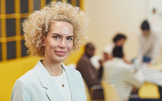 A businessperson in a blazer stands for a team portrait in a modern office setting