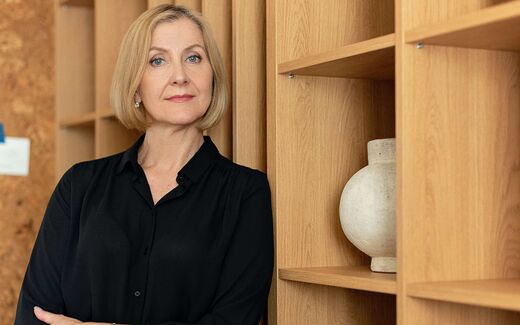 A senior executive in a dark blouse standing by wood shelving, a generic stand-in for AbbVie leadership