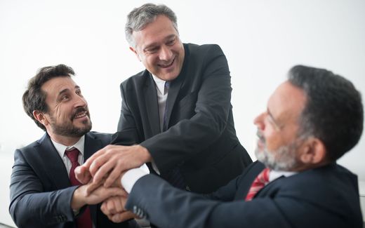 Three executives in business suits clasp hands together in a celebratory gesture